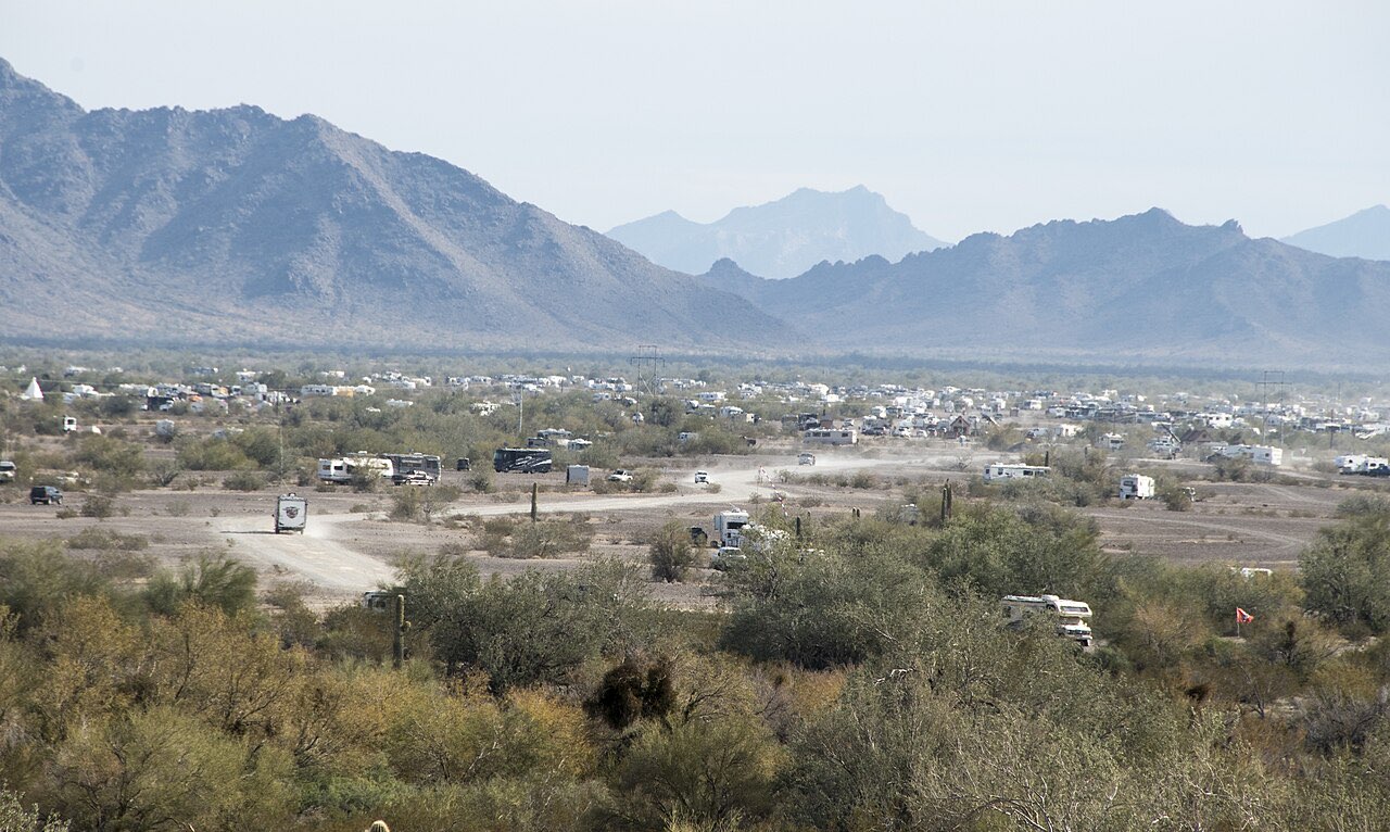 Hundreds of RVs spread across open desert at the La Posa Long Term Visitor Area near Quartzsite, Arizona, with mountains behind