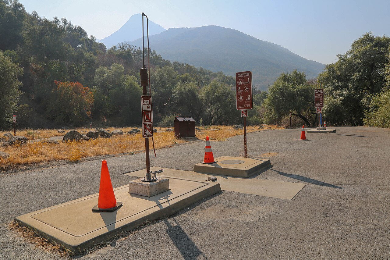 Concrete pad dump station with two orange traffic cones and brown National Park Service instruction signs, with hills and oak trees behind