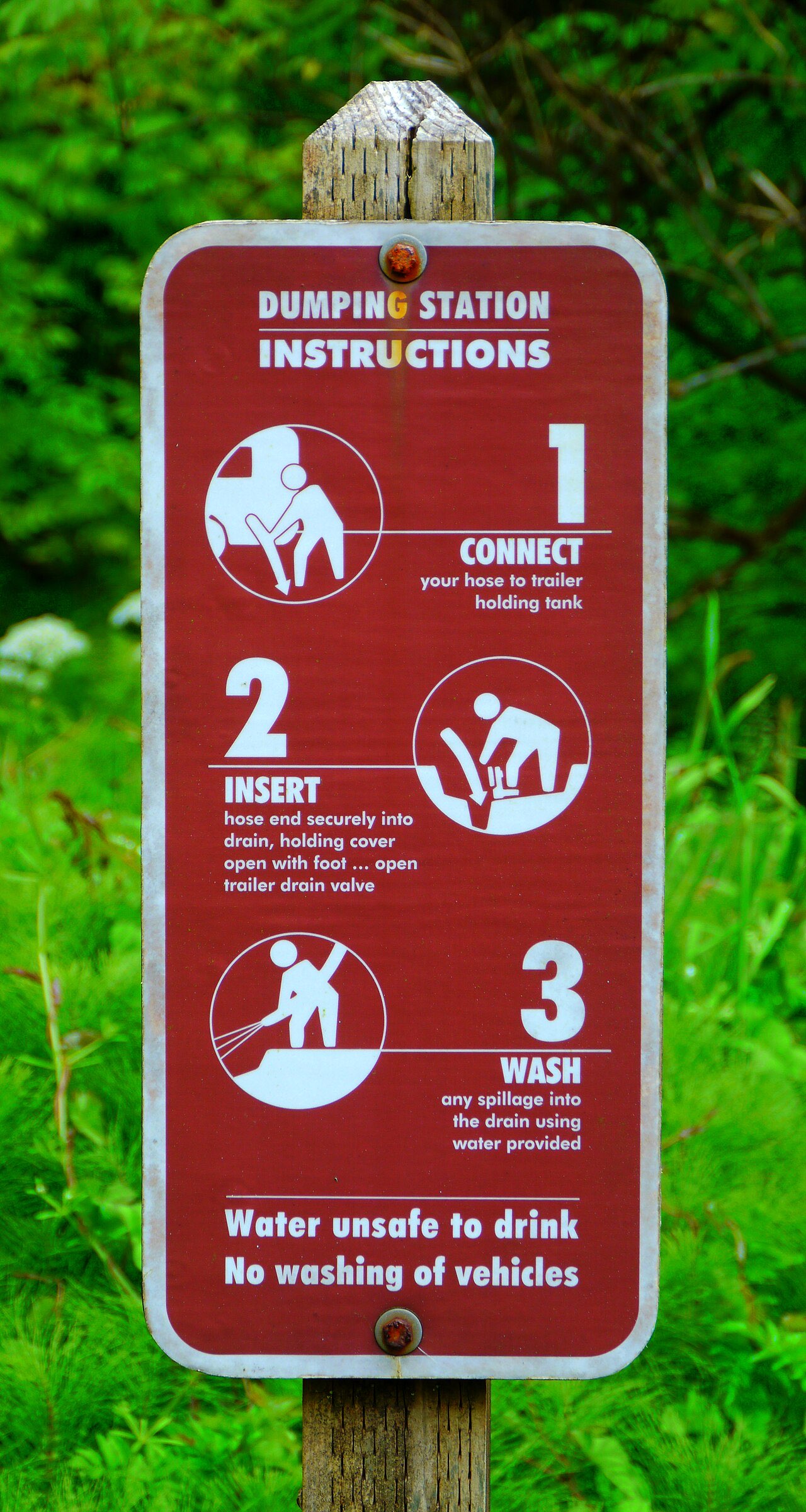 Brown wooden-post sign reading Dumping Station Instructions with three numbered pictograms: connect, insert and wash, and a warning that the water is unsafe to drink