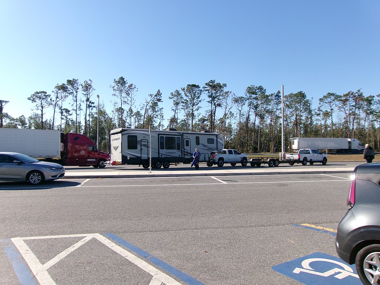 A white pickup towing a fifth-wheel toy hauler parked in the truck lane of an interstate rest area