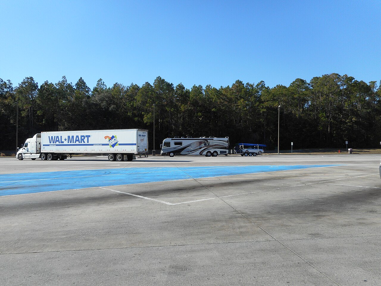 A Class A motorhome towing a trailer parked next to a semi truck at an interstate rest area
