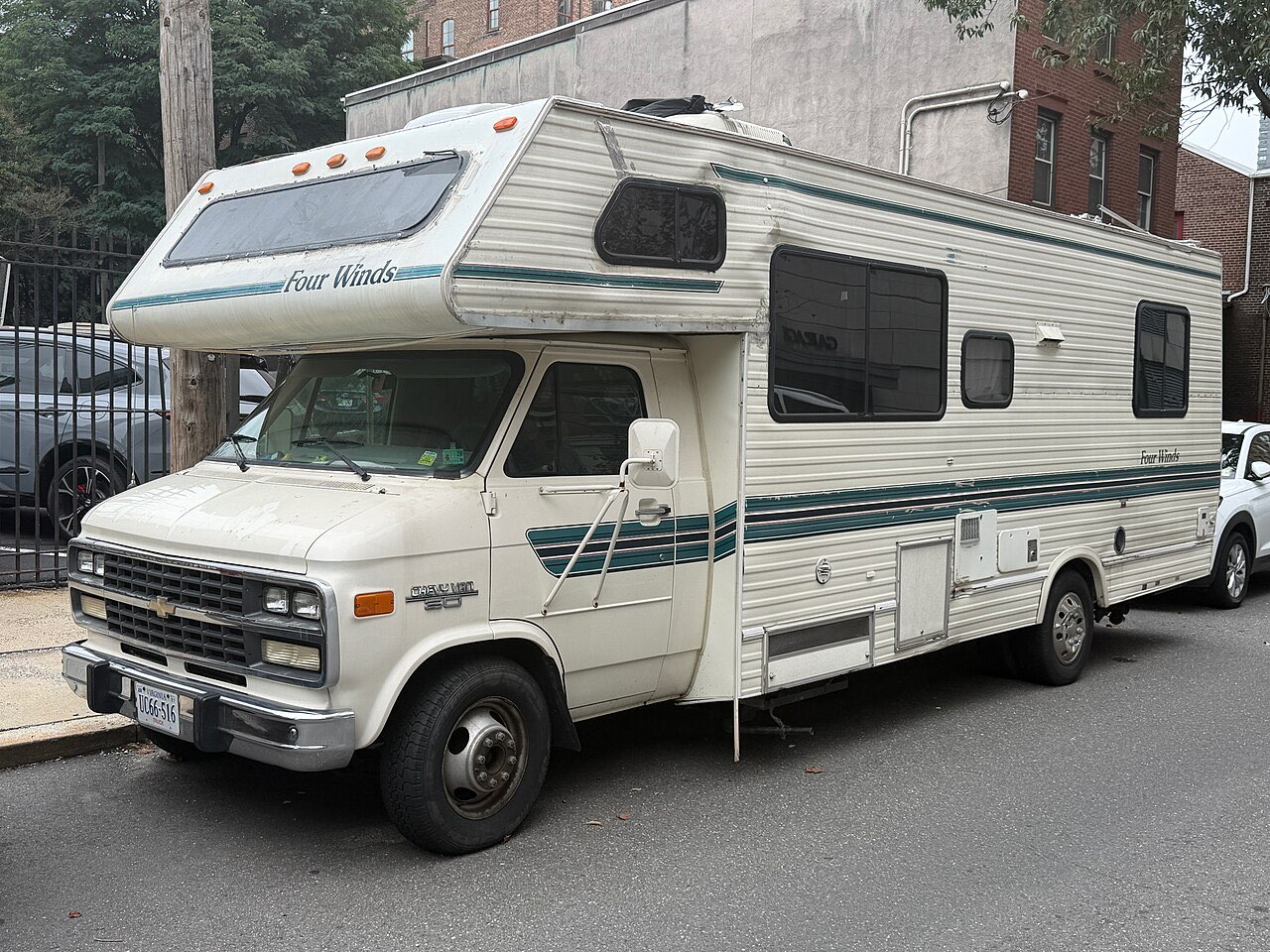 White 1994 Four Winds Class C motorhome with a cab-over bunk, built on a Chevrolet van chassis, parked on a city street